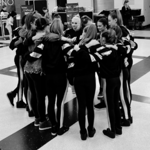 Dance team huddled in a circle with teammates, sharing a moment of camaraderie before their stage performance