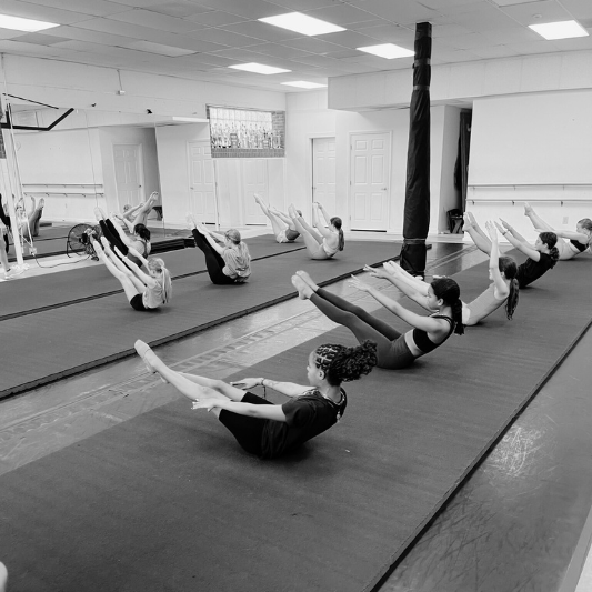 Dedicated dancers engaging in core-strengthening exercise on tumbling mats during a conditioning session at Charleston Dance Center.